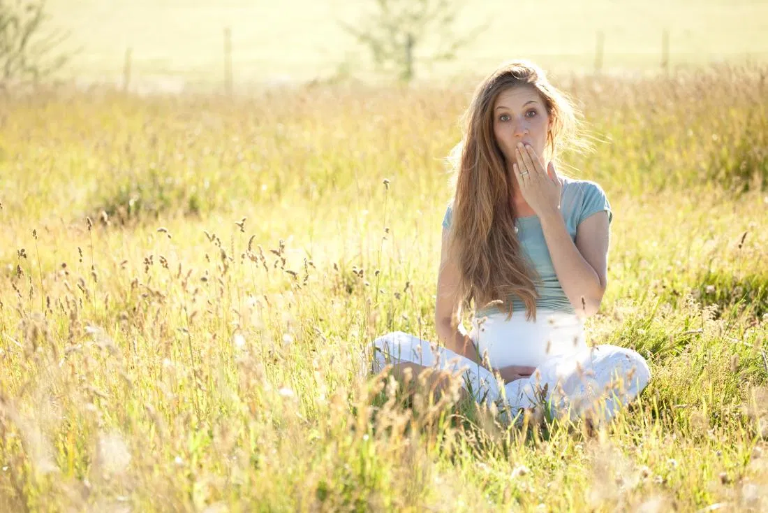 pregnant_woman_sitting_in_a_meadow_with_hand_up_to_her_mouth.jpg
